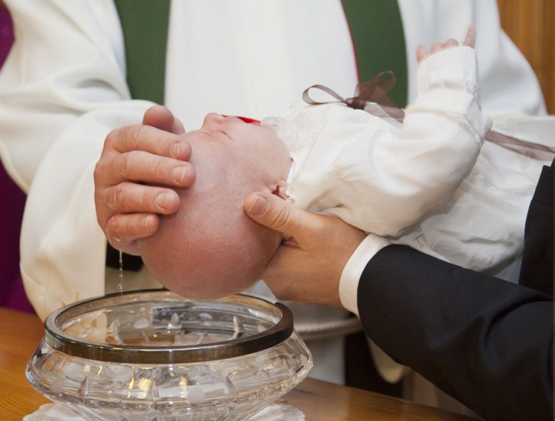 La persona que sostiene al bebé que recibe el agua bautismal del sacerdote, como signo de creencia religiosa.