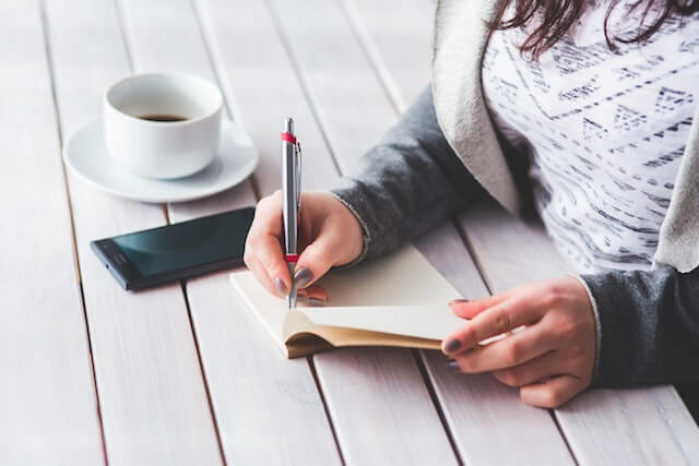 Mujer escribiendo en un diario con una taza de caf&eacute;