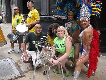 Se ve a siete personas en el Desfile del Orgullo por Discapacidad anual de Chicago en 2011. En el centro, una mujer con una discapacidad f&iacute;sica visible se sienta junto a un andador mientras otros asistentes disfrazados sostienen instrumentos a su alrededor.