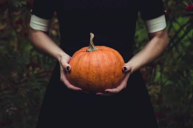 persona sosteniendo una calabaza y vistiendo un vestido negro y esmalte de u&ntilde;as negro