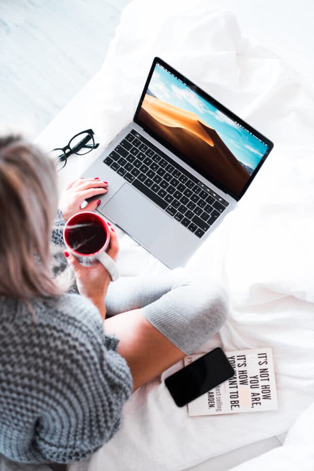 Mujer sosteniendo una taza de caf&eacute; y trabajando en un port&aacute;til