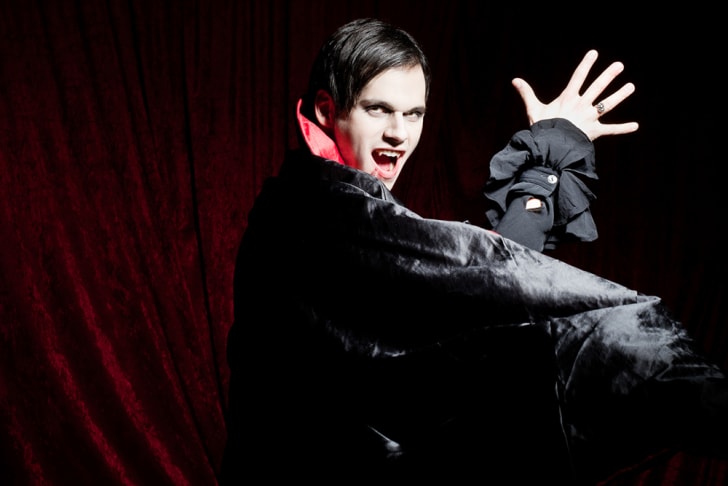 Un vampiro masculino dram&aacute;tico en una capa de terciopelo mostrando sus dientes