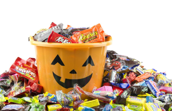 Un cubo naranja lleno y rodeado de dulces de Halloween.