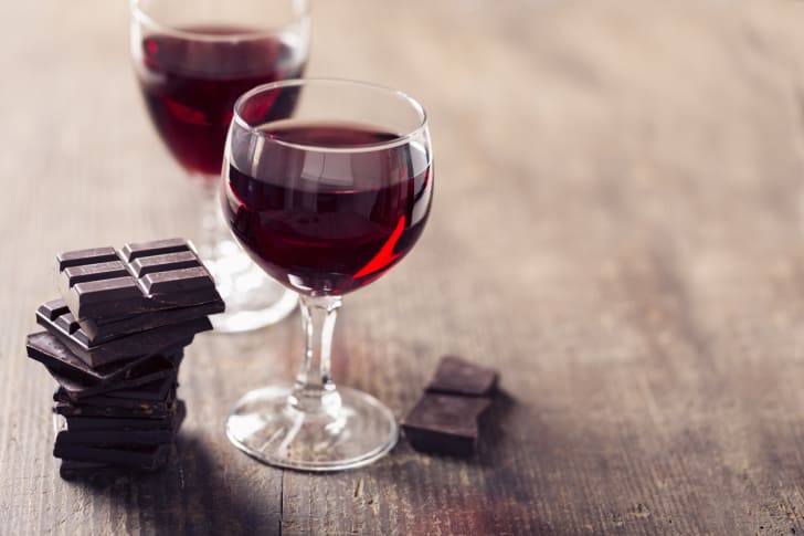 Dos clases de vino tinto sobre una mesa con un poco de chocolate.