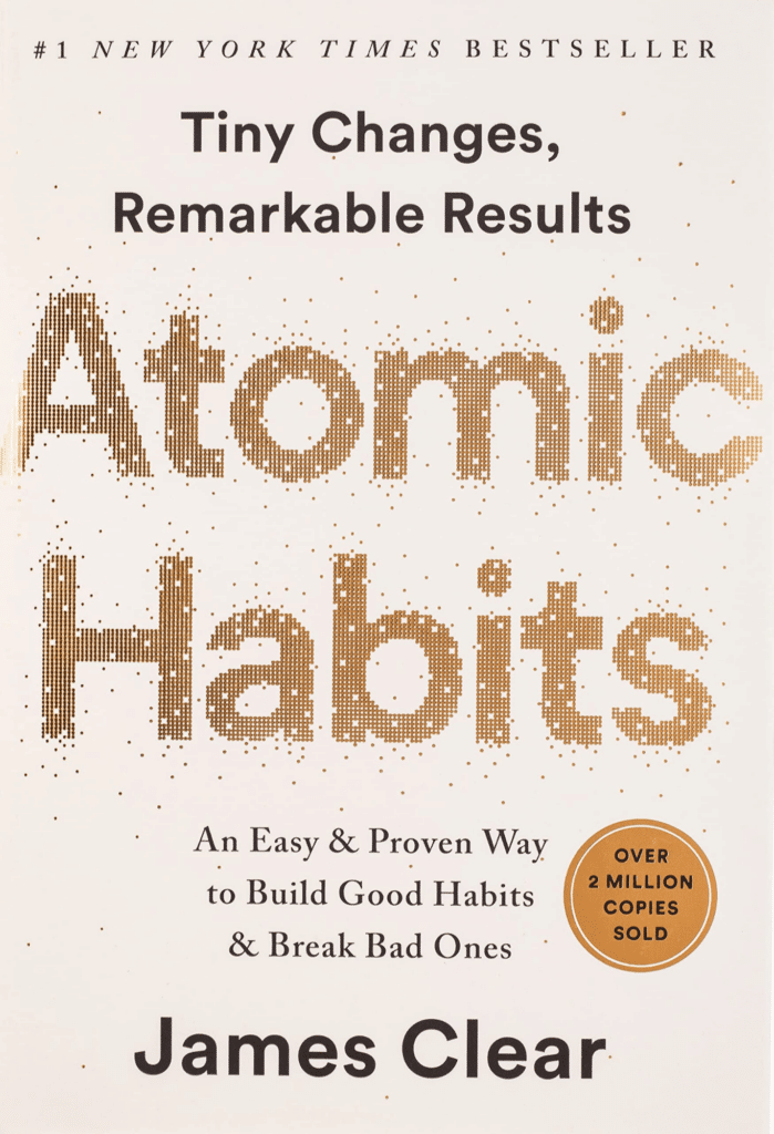 Su guía de los 10 mejores libros de negocios de todos los tiempos Portada del libro Atomic Habits de James Clear con el título en texto dorado grande.